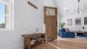 A modern living room with a wooden bench, a blue sofa, and a wooden door. - Pelican Landing At The Bay (Pensacola)