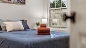 A neatly made bed with a blue bedspread and three brown towels stacked in the center. - Pelican Landing At The Bay (Pensacola)