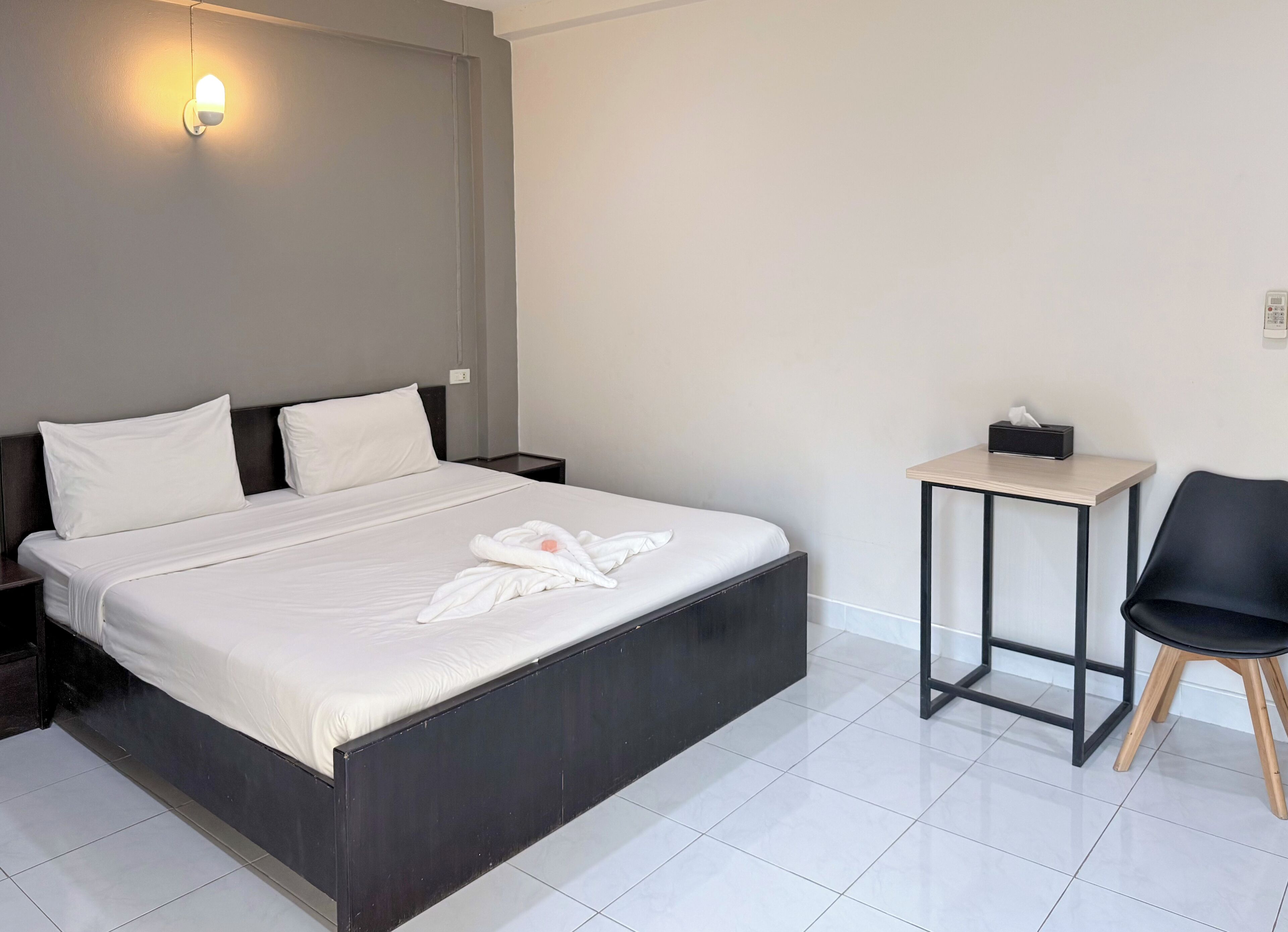 Habitación de hotel con una cama grande, una mesita de noche con caja de pañuelos, una silla y una lámpara de pared.