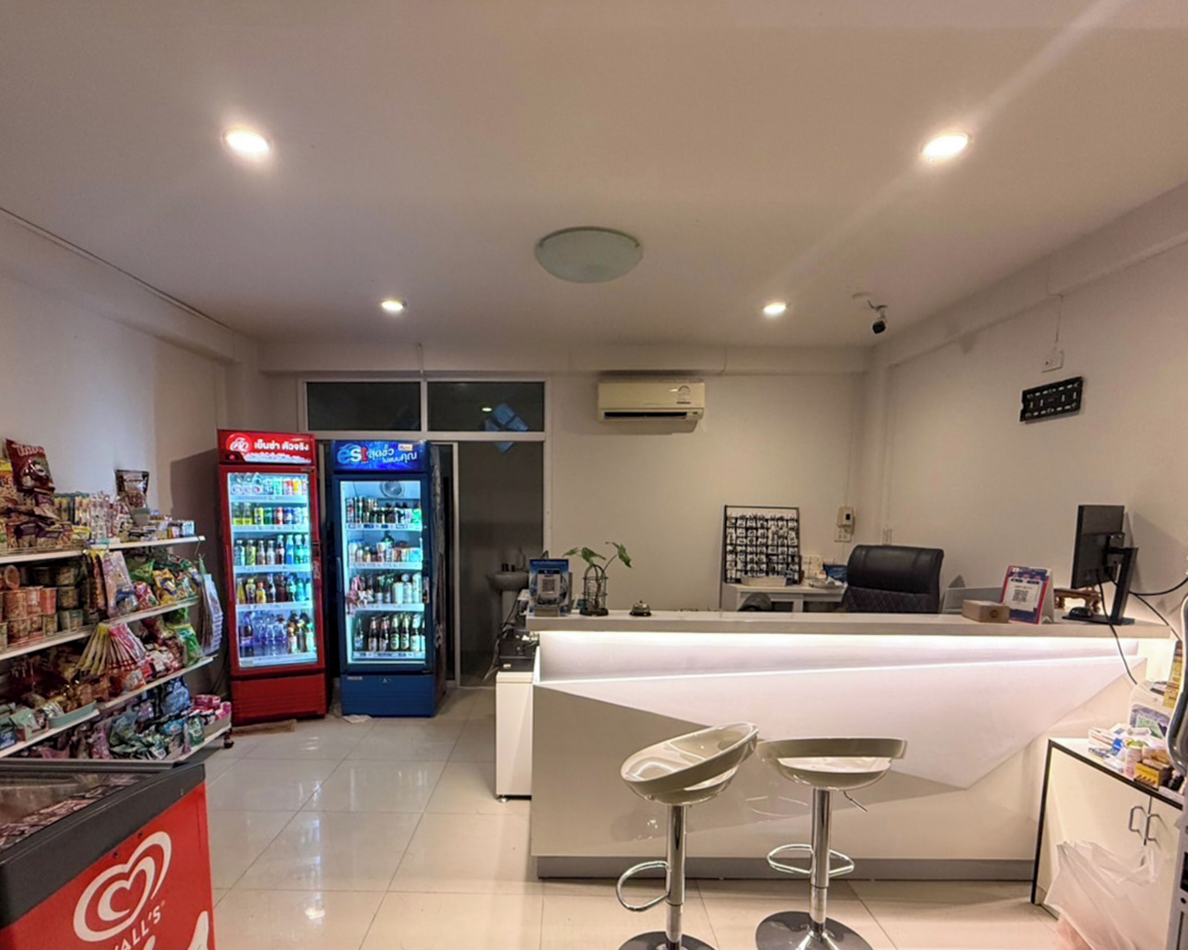 Un área de recepción con mostrador, dos taburetes tipo bar, máquina expendedora y refrigerador.