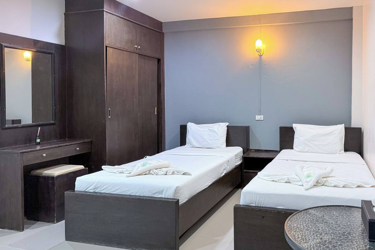 Habitación de hotel con dos camas, un armario de madera oscura, un escritorio pequeño y una mesa redonda.
