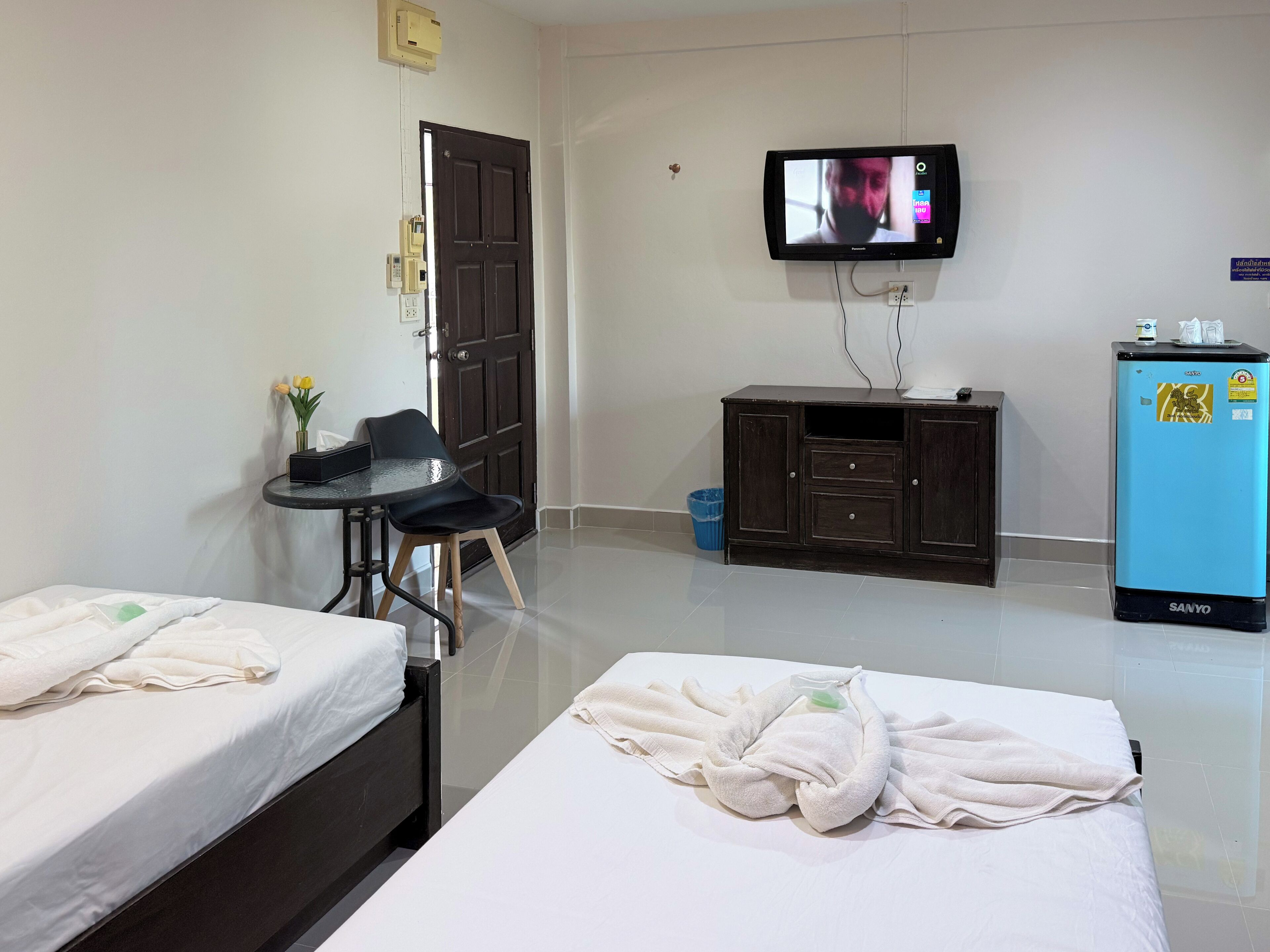 A hotel room with two beds, a small table with chairs, a television, a minibar, and a trash bin.