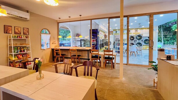 Un restaurante con mesas y sillas de madera, una barra y vistas a una lavandería a través de amplios ventanales.