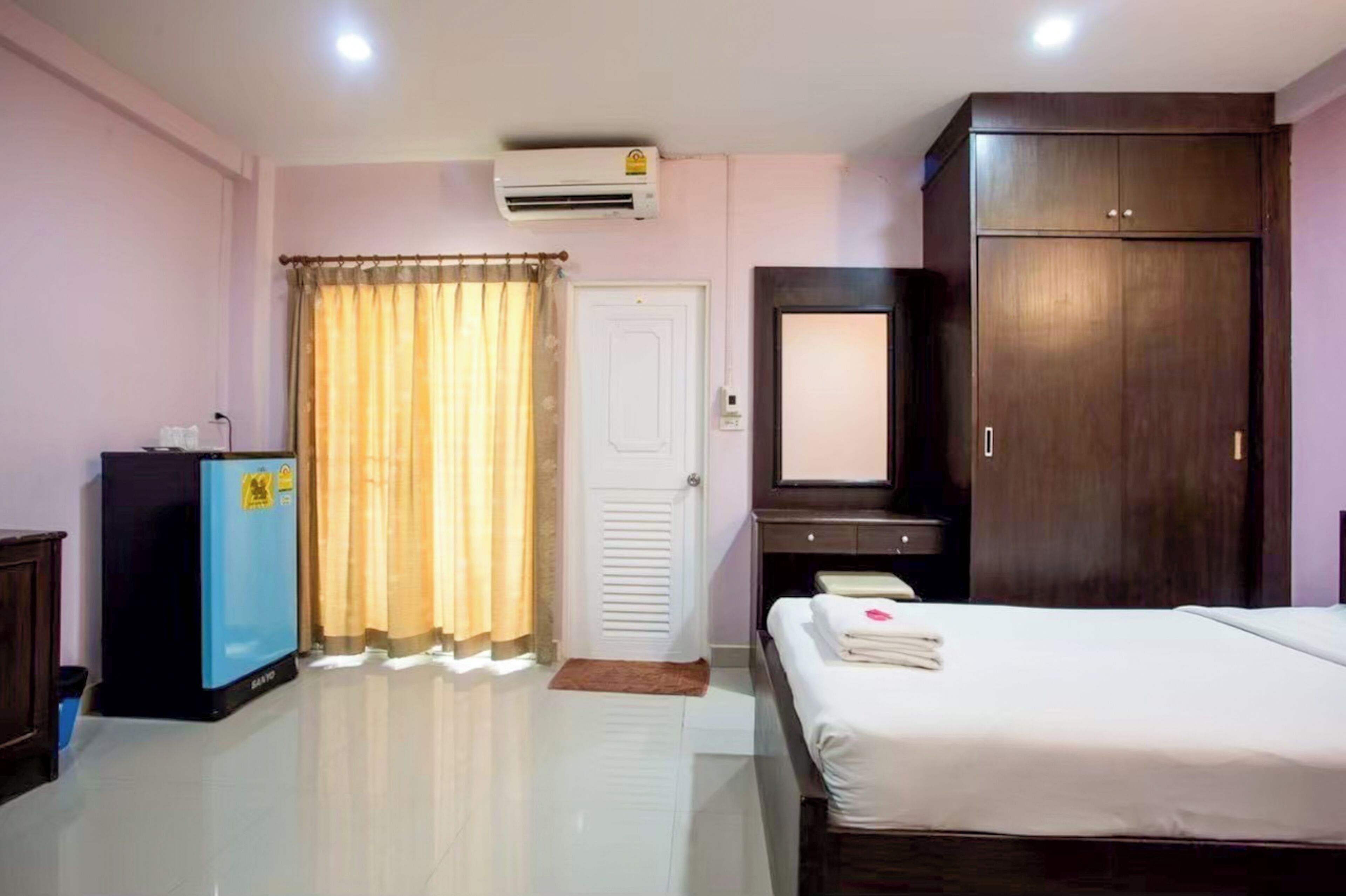 Una habitación de hotel con cama, armario, espejo, escritorio con computadora y aire acondicionado.