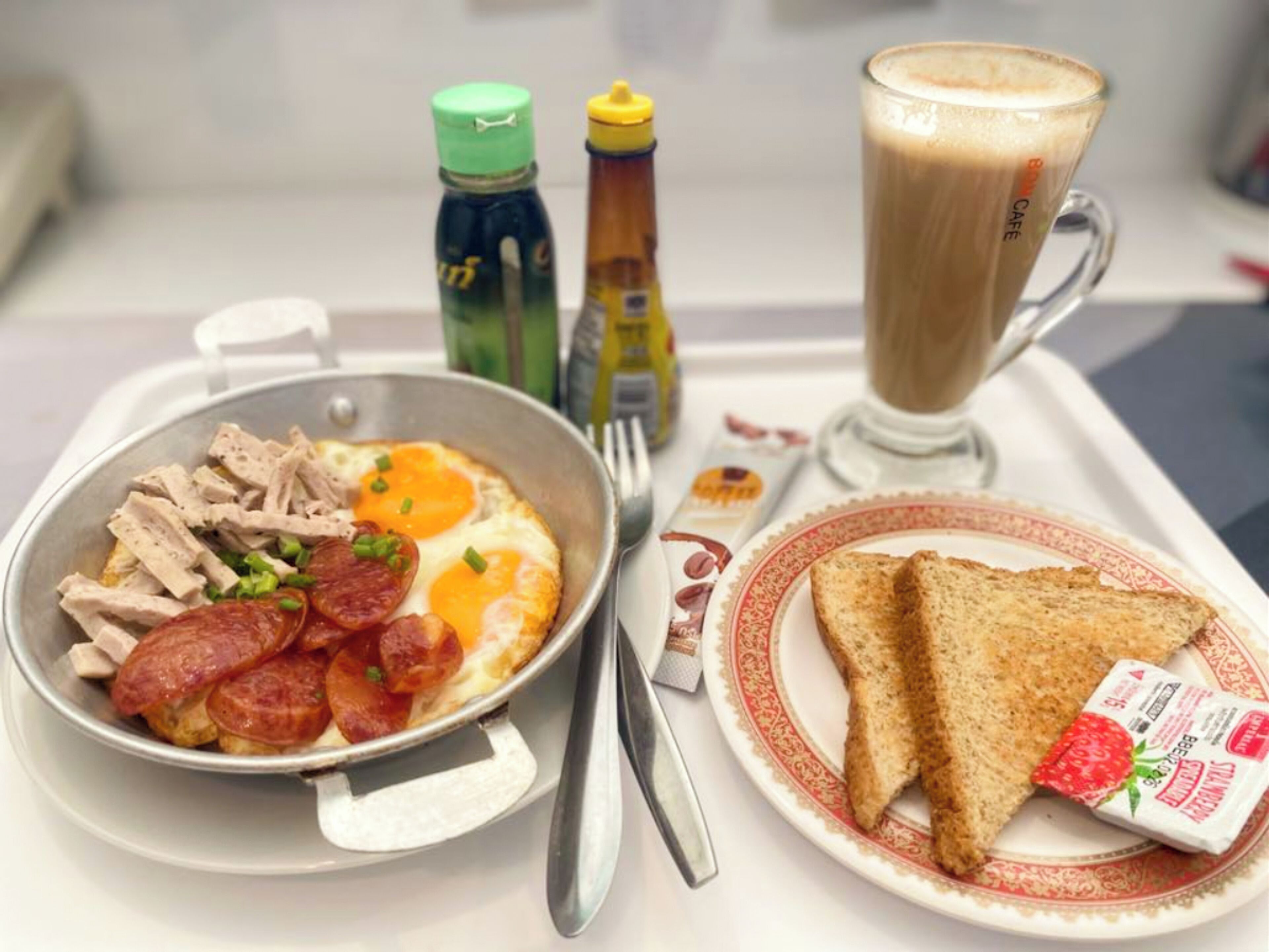 A breakfast tray with scrambled eggs, turkey slices, and sausage, a glass of coffee, toast, and a strawberry jam packet.