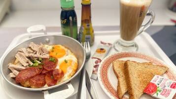 A breakfast tray with scrambled eggs, turkey slices, and sausage, a glass of coffee, toast, and a strawberry jam packet.