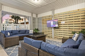 A covered outdoor seating area with wicker furniture, a flat-screen TV, and a wooden slat wall. - 6BR Retreat w/ Pool + Hot Tub | Sleeps 24 (North Myrtle Beach)