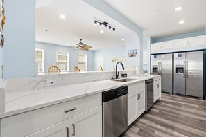 A modern kitchen with white cabinetry, a dishwasher, a double sink, and a stainless steel refrigerator. - 6BR Retreat w/ Pool + Hot Tub | Sleeps 24 (North Myrtle Beach)