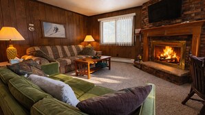 Ein gemütliches Wohnzimmer mit Kamin, Holzwänden, einer Couch, einem Couchtisch und zwei Lampen.