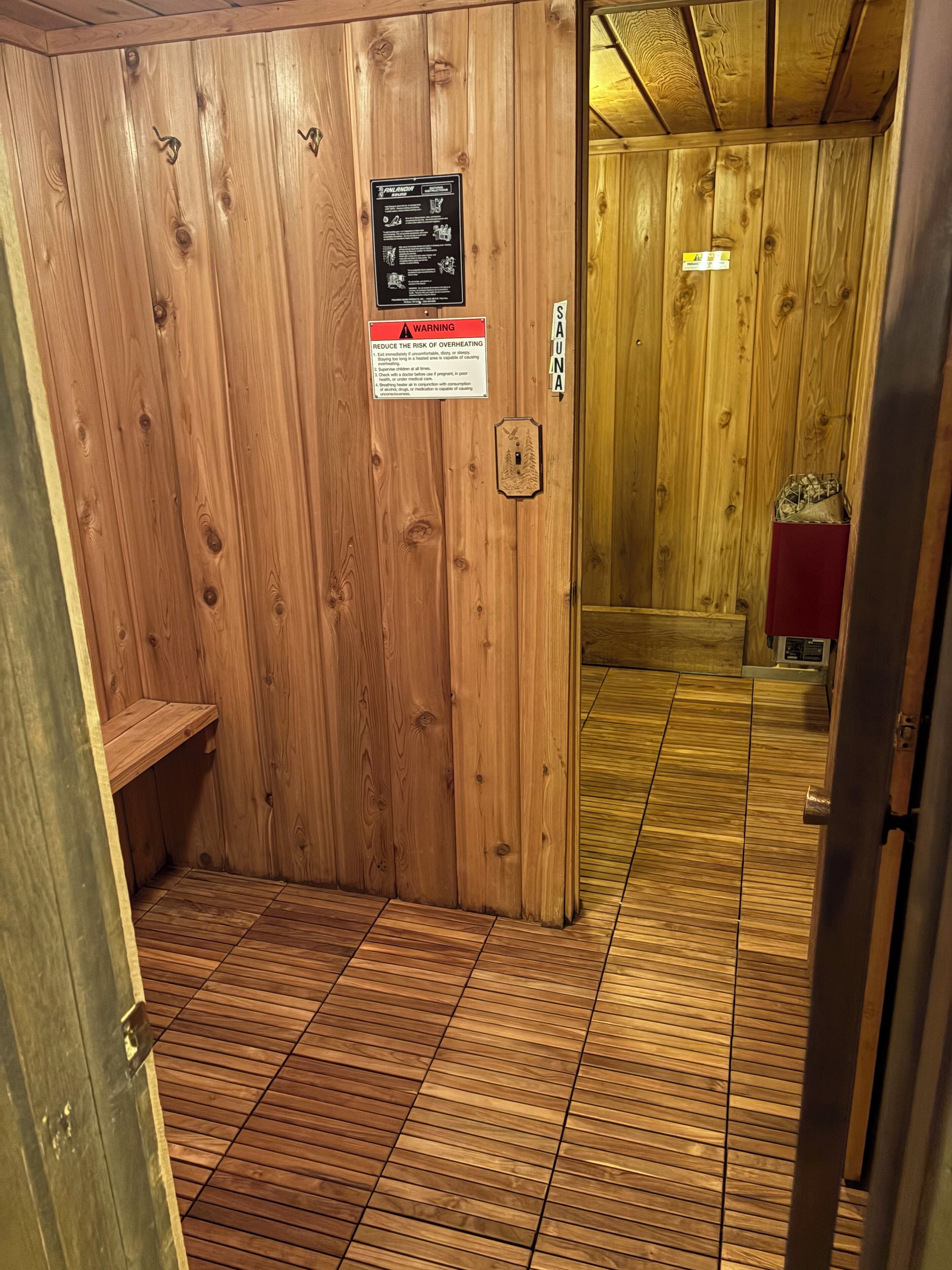 Interior de madeira com um aviso, uma porta com puxador e piso ladrilhado.