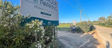 A sign for 'PRAQUE PARKING' with 'PRAIAS DE CACELA' and 'Praia da Fabrica' text, indicating a parking area near a natural setting.
