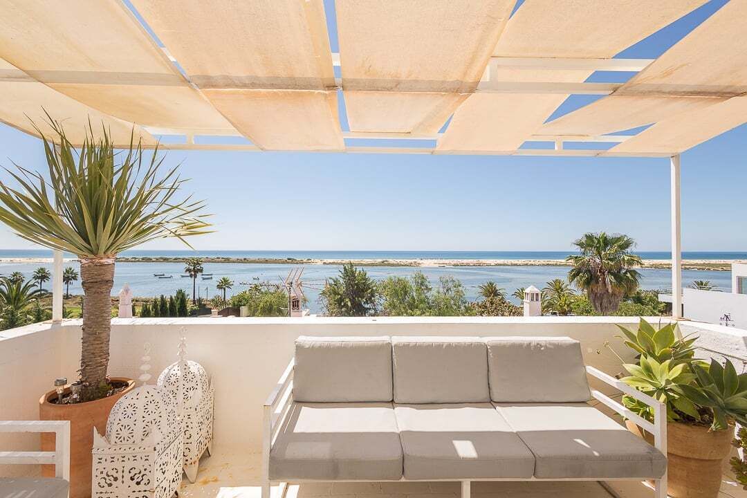 Ein Balkon mit einer weißen Couch, einer Palme und Blick aufs Meer.