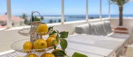 A three-tiered metal fruit stand with lemons and leaves on a white table by a seaside view.