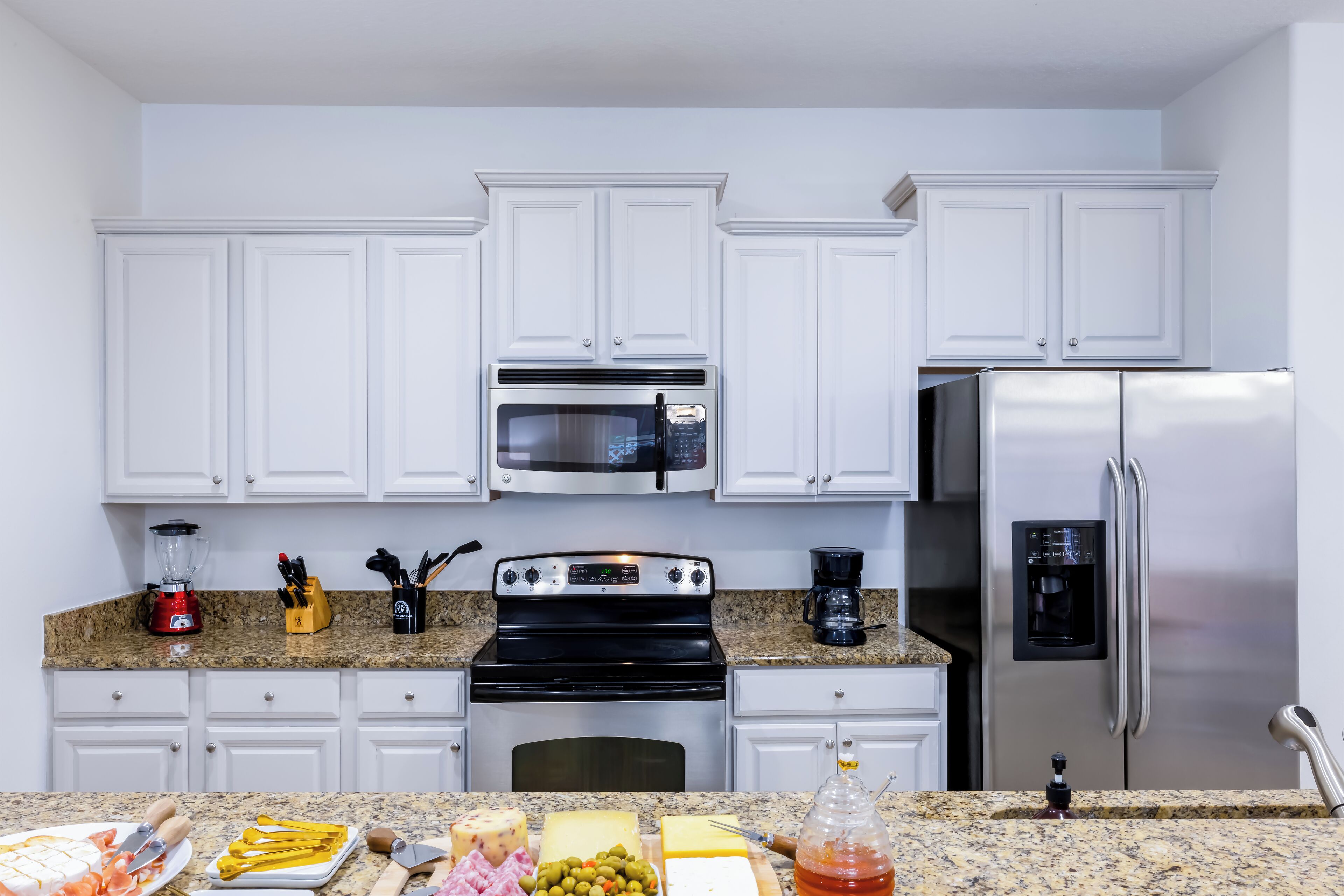 A kitchen with white cabinets, a stainless steel refrigerator, a microwave, and a stove.