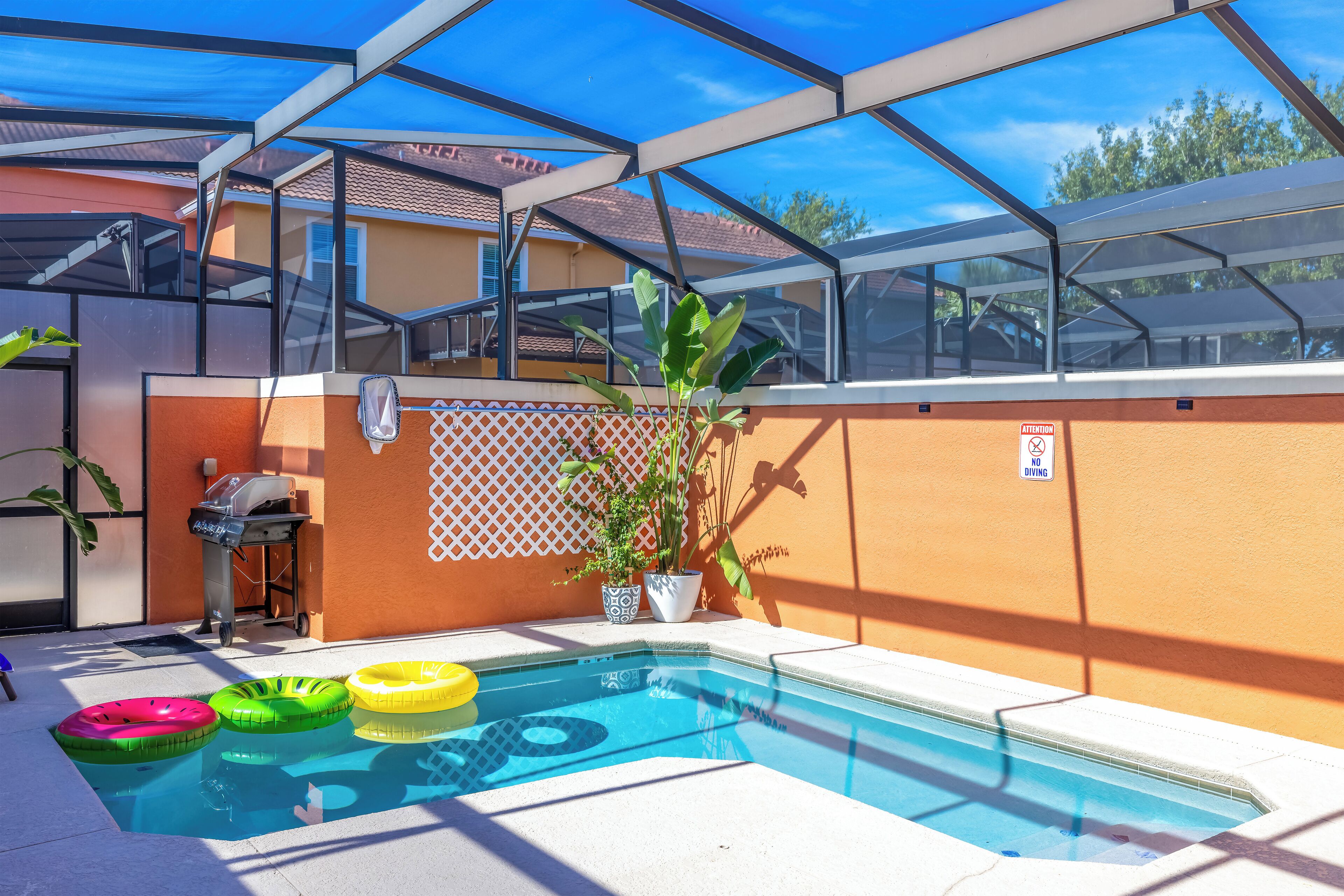 A swimming pool with a glass enclosure, surrounded by a patio area with a grill and potted plants.
