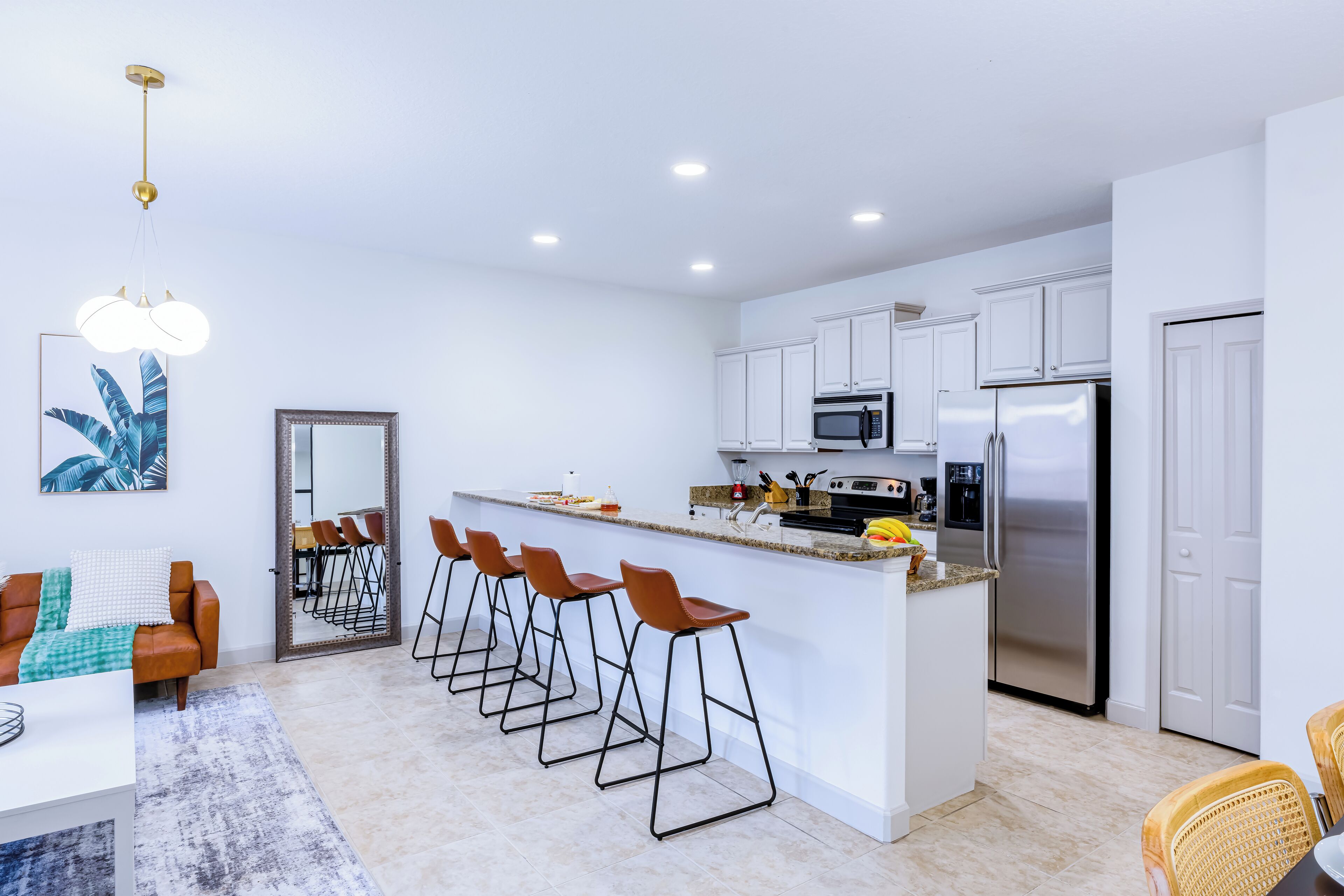A modern kitchen with white cabinets, a stainless steel refrigerator, and a bar area with stools.