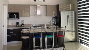 Une cuisine moderne dotée d’un îlot central, d’appareils électroménagers en acier inoxydable et d’un coin repas avec des tabourets de bar.