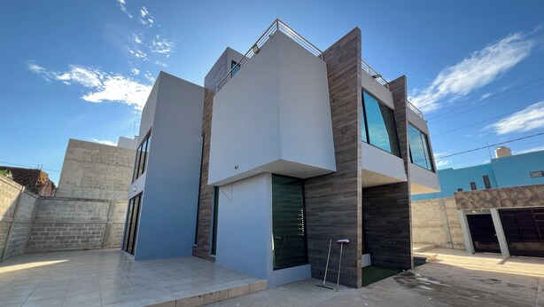 Une maison moderne à deux étages, dotée d’un toit plat, de grandes fenêtres et d’une terrasse en béton.
