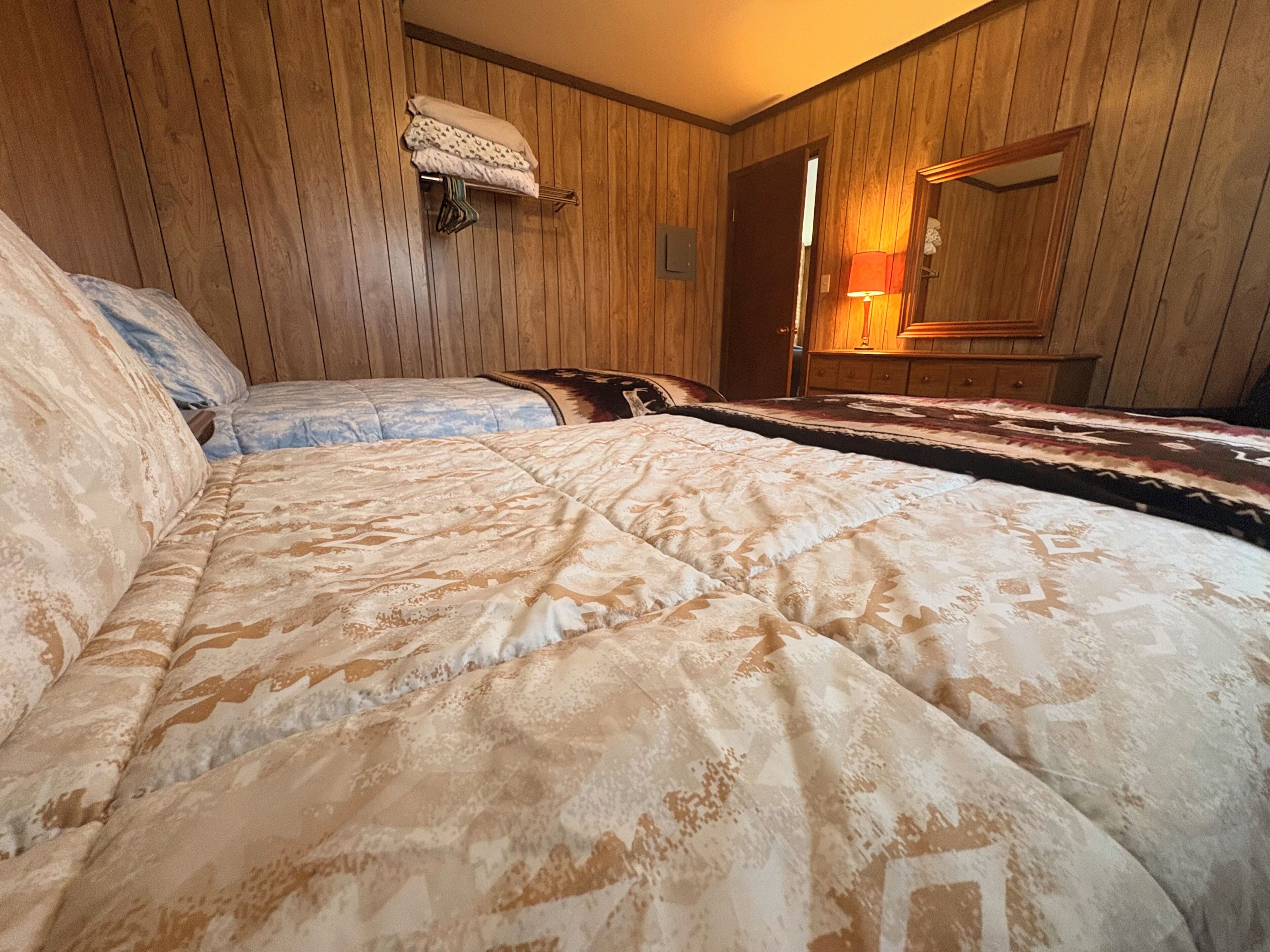 A room with wooden paneling, a bed with patterned bedding, a hanging towel rack, and a mirror.