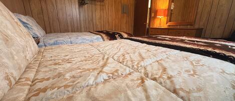 A room with wooden paneling, a bed with patterned bedding, a hanging towel rack, and a mirror.