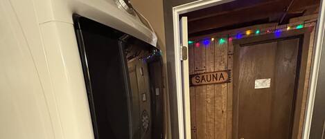 A sauna room with a wooden door labeled "SAUNA" and a white sauna machine.