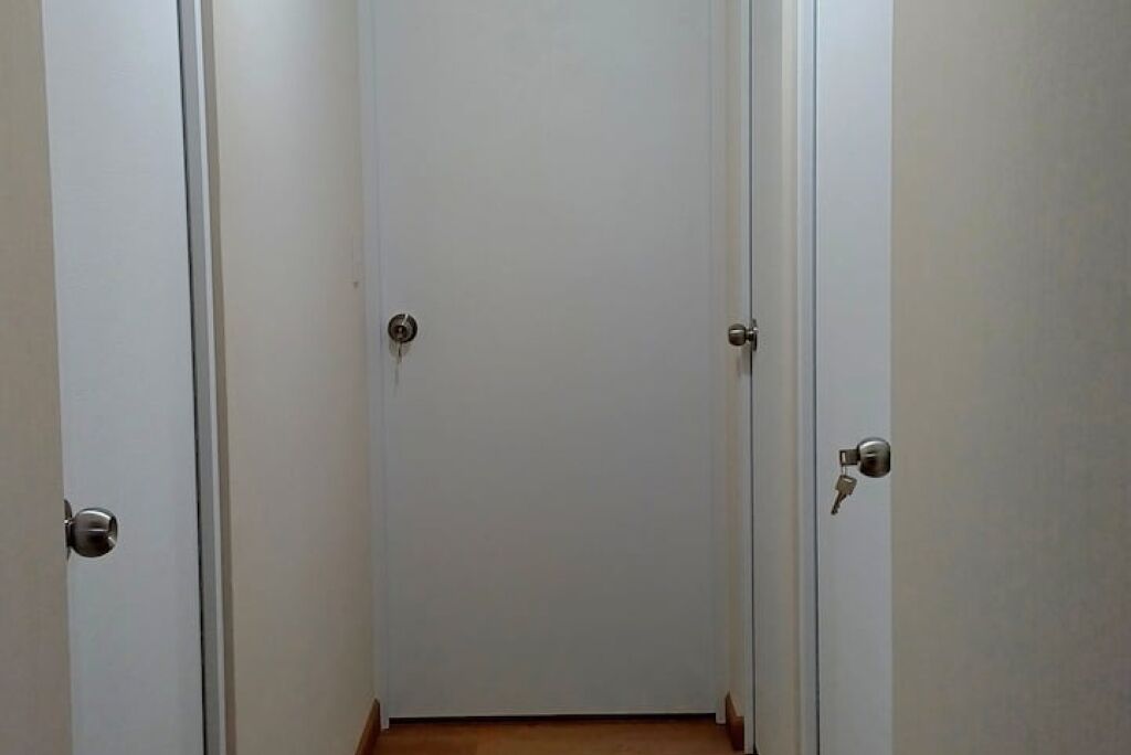 A narrow hallway with three white doors, each with a keyhole and a round handle.