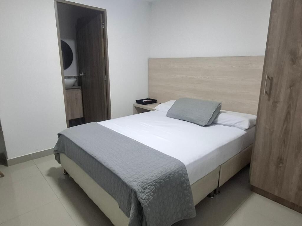 A bedroom with a bed, a nightstand, a wooden headboard, and a wardrobe.