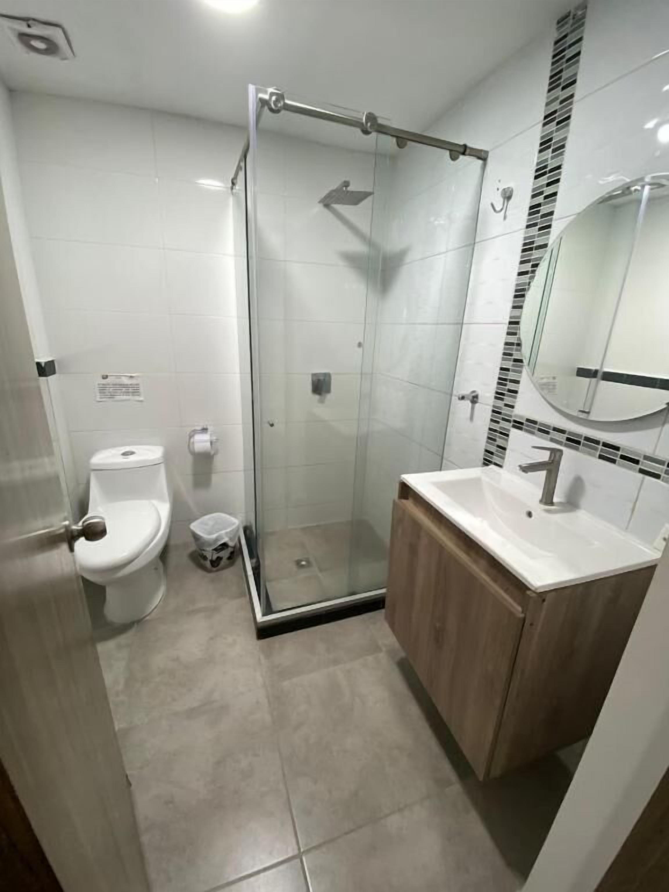 A modern bathroom with a glass-enclosed shower, a toilet, and a sink with a wooden cabinet.