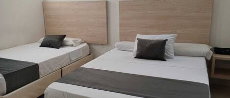A hotel room with two single beds, a wooden headboard, a small bedside table, and a window with a view of trees.