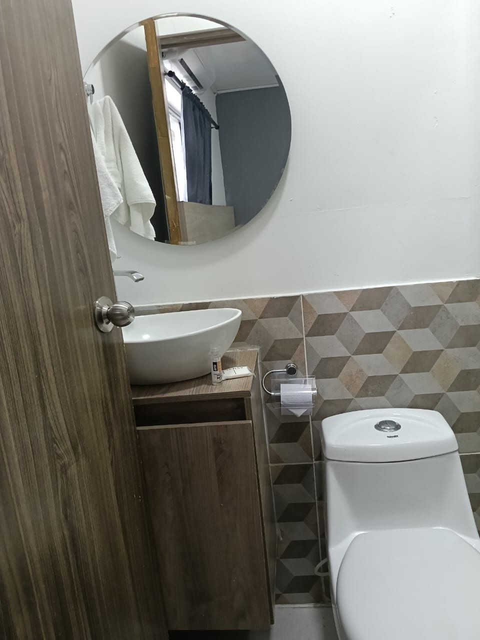 A bathroom with a round mirror, a white sink, a toilet, and a wooden cabinet.