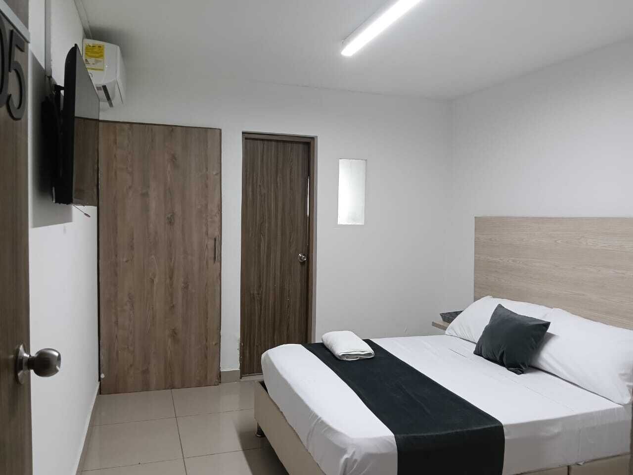 Une chambre à coucher avec un lit, une porte en bois, un mur blanc et un luminaire au plafond.