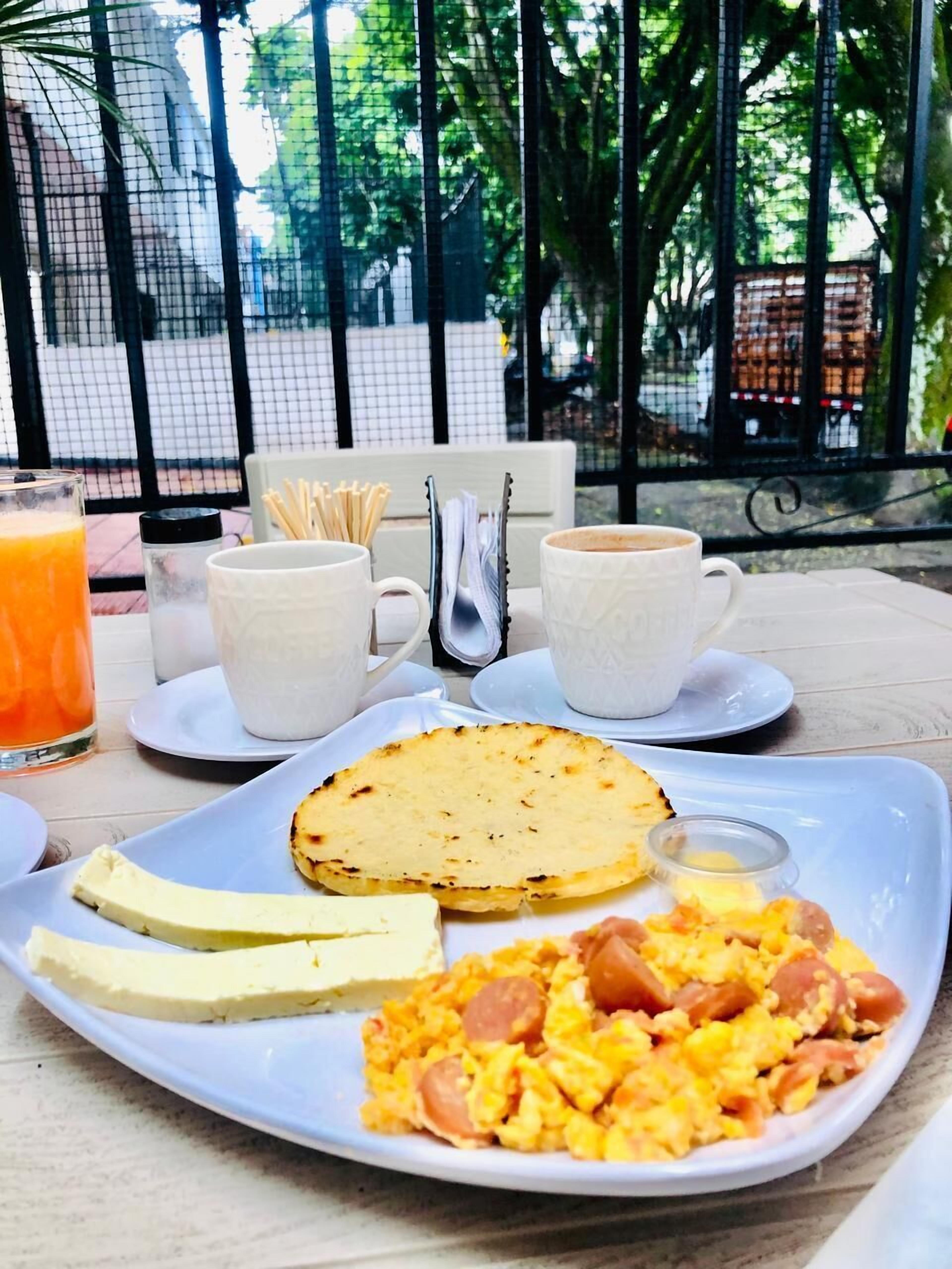 A breakfast tray with eggs, toast, and juice on a table with a view of trees and a fence.