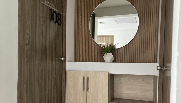 A wooden door with a number plate, a mirror, and a small plant on a white shelf. - Hotel Pasarela Real Cail (Cali)