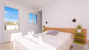 Ein Schlafzimmer mit einem Bett, einem Fenster, einem Nachttisch mit einer Pflanze und einer Wandleuchte.
