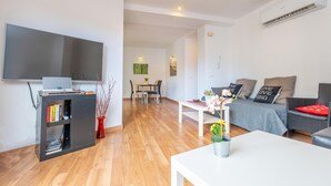 A modern living room with a flat-screen TV, a bookshelf, a dining area with a table and chairs, and a sofa with decorative pillows. - RESIDENCIAL SUITES VALLDEMOSSA - S'Arxiduc (Valldemossa)