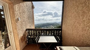 Un balcón con una mesa y sillas, vista a un paisaje con colinas y cielo nublado.