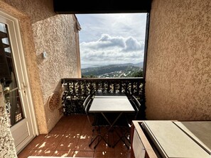 Ein Balkon mit Tisch und Stühlen, Blick auf eine Landschaft mit Hügeln und bewölktem Himmel.