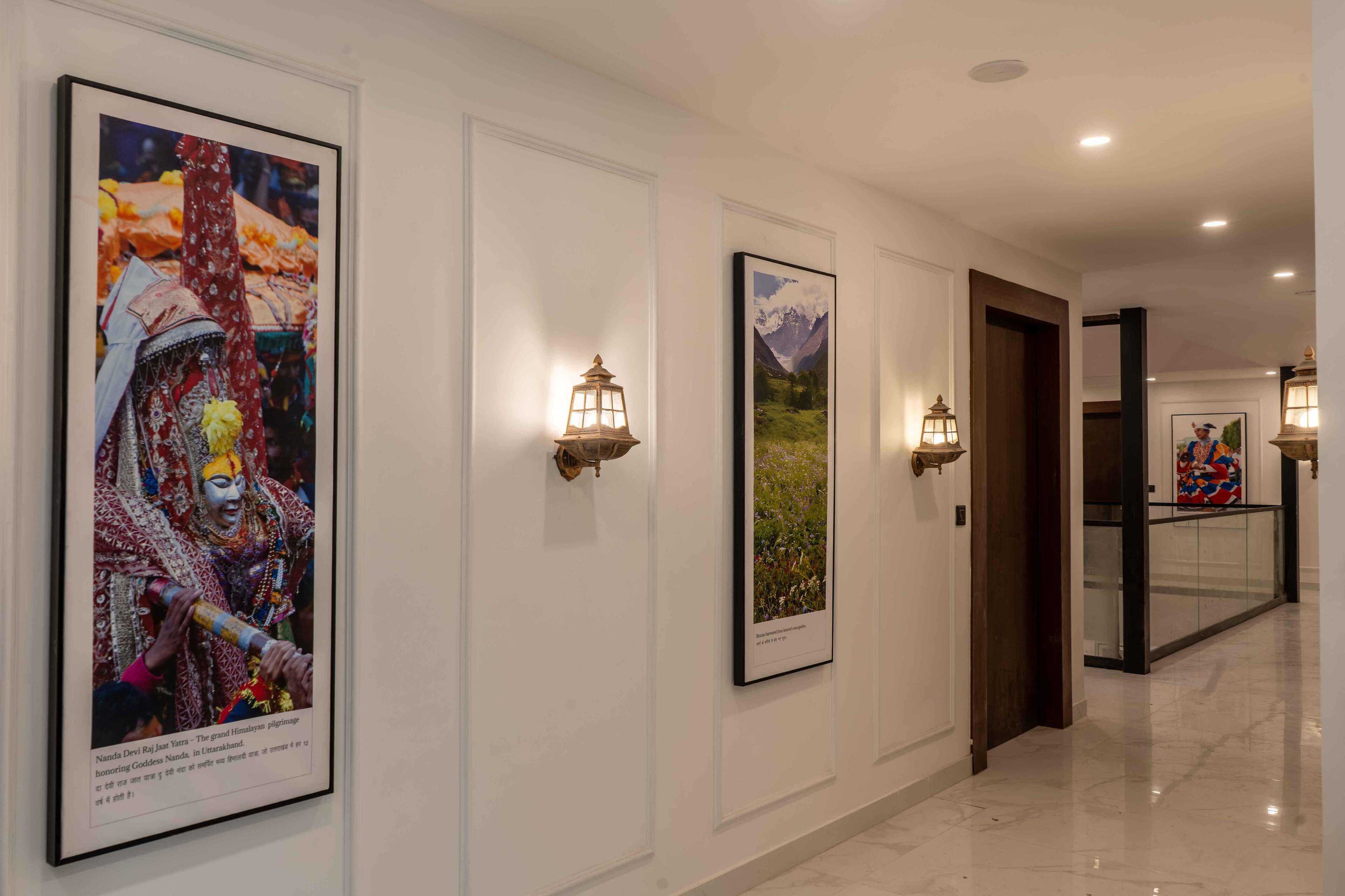 A hallway with framed artwork on the walls, wall-mounted lanterns, and a polished marble floor.