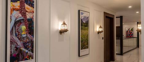 A hallway with framed artwork on the walls, wall-mounted lanterns, and a polished marble floor.