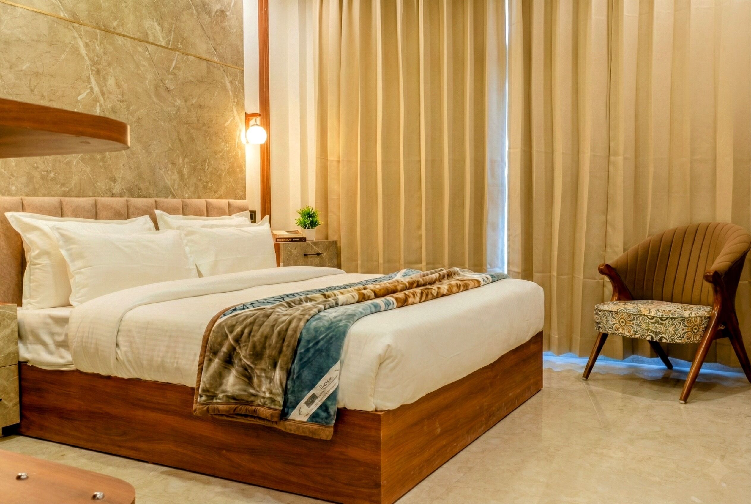 Un dormitorio con una cama de madera, una mesita de noche con una lámpara, una silla y una ventana con cortinas.