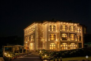 A multi-story building with a symmetrical facade, large windows, and a central entrance with steps. - Suryoday The Vaikunth (Badrinath)