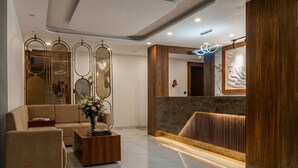A modern lobby with a reception desk, a sofa, a coffee table, and decorative panels. - Suryoday The Vaikunth (Badrinath)
