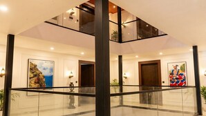 A spacious lobby with a glass railing, a high ceiling, and artwork on the walls. - Suryoday The Vaikunth (Badrinath)