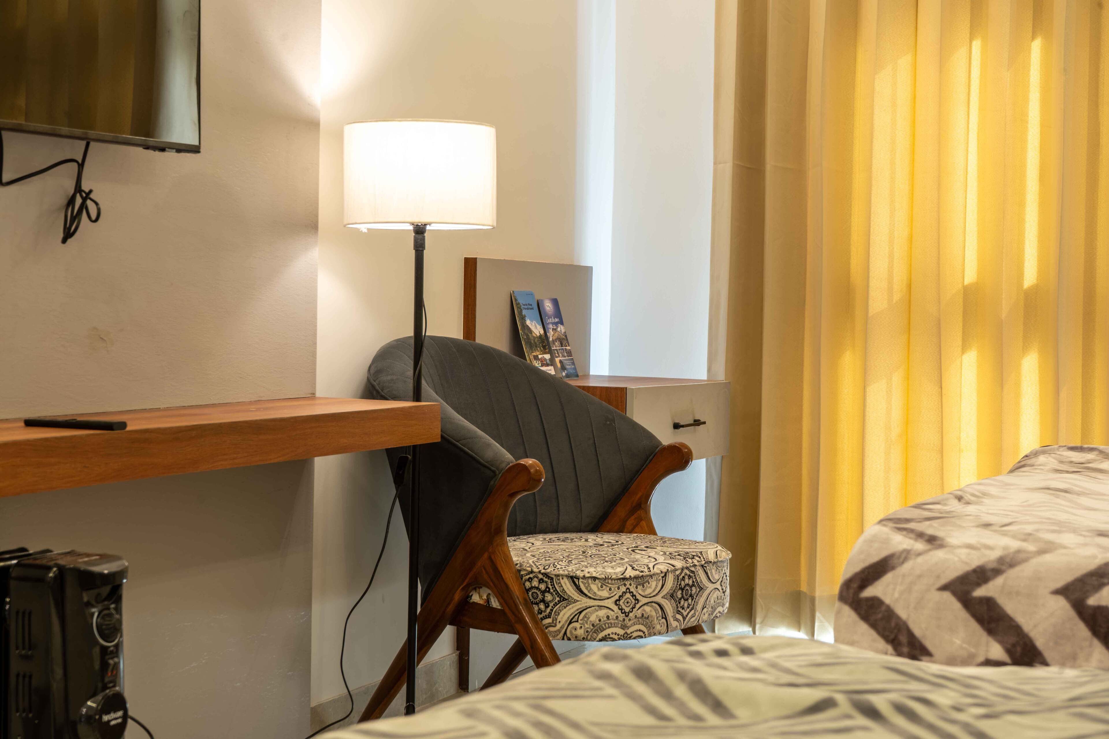 A hotel room with a bed, a desk with a lamp, a chair, and a television mounted on the wall.