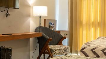 Una habitación de hotel con cama, escritorio con lámpara, silla y televisión montada en la pared.