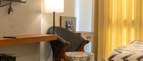 A hotel room with a bed, a desk with a lamp, a chair, and a television mounted on the wall.