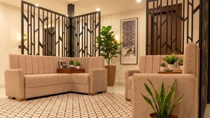 A modern living room with a beige sectional sofa, a matching armchair, and a patterned floor. - Suryoday The Vaikunth (Badrinath)