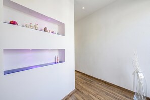 A room with two white walls, a wooden floor, and a shelf with various items. - Asia Apartment 2BR in Laveno Center (Laveno Mombello)