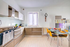 A modern kitchen with a central island, built-in oven, and a dining area with a glass table and chairs. - Asia Apartment: 2BR in Laveno Center (Laveno Mombello)