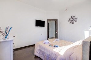 Ett hotellrum med en säng, en tv som är monterad på väggen, en spegel och en vägg med fotografier.